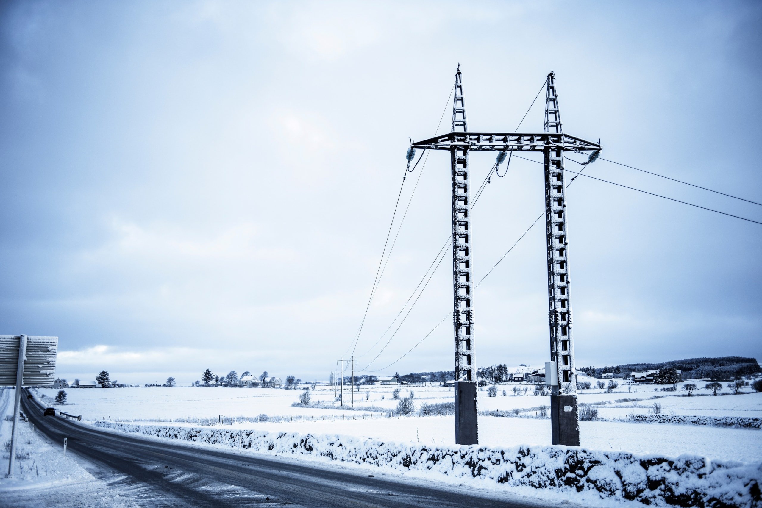 Kraftlinje på Jæren over et snøkledd jorde og langs en bilvei. Foto