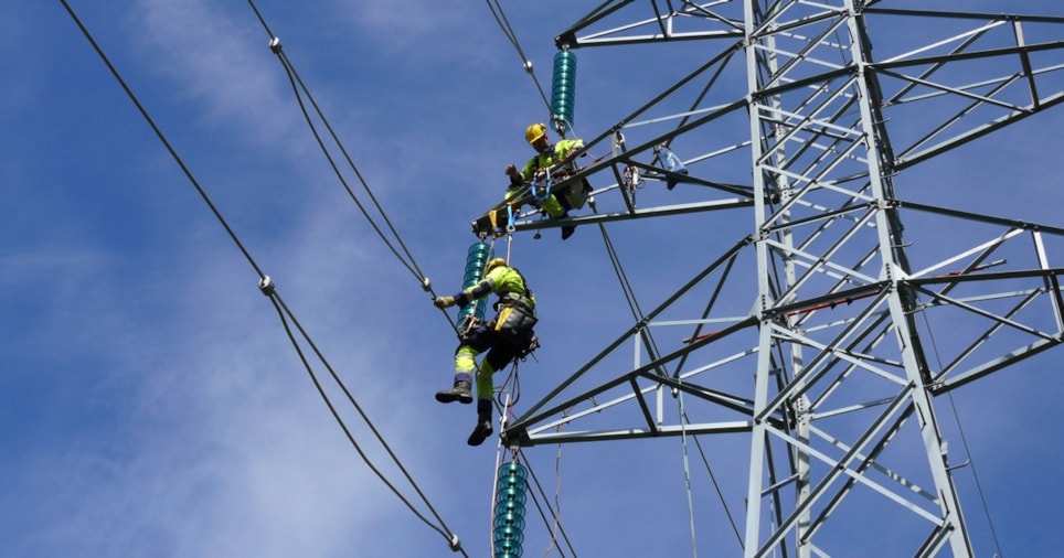 To energimontører klatrer i en kraftmast.