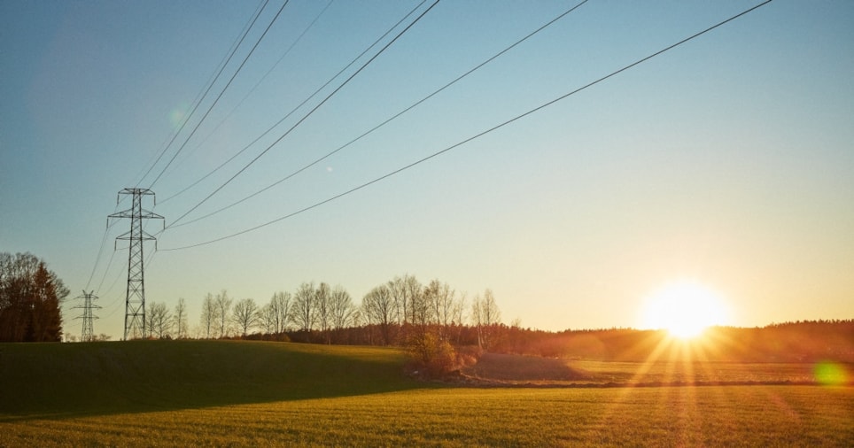 Strømmast over et jorde i solnedgang