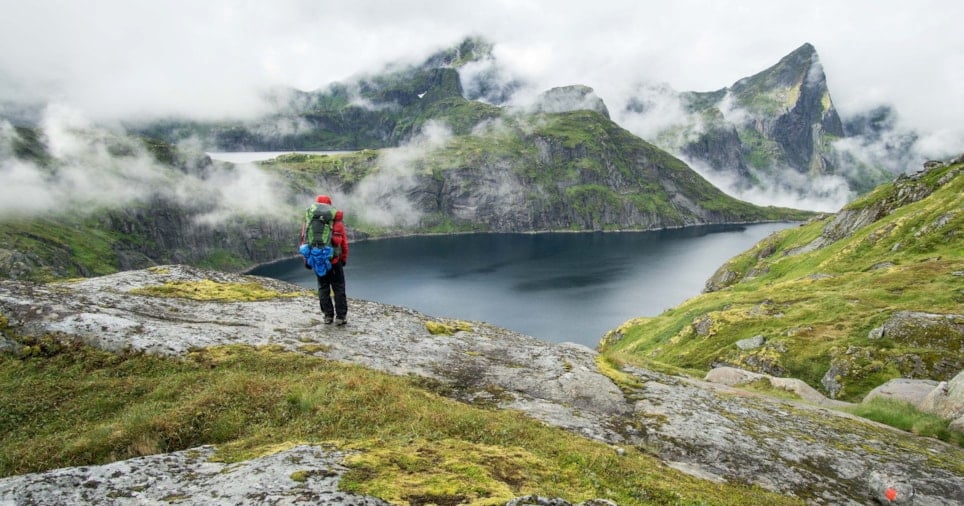 Person med stor ryggsekk ser utover fjell og vann. Foto