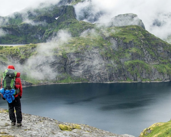 Person med stor ryggsekk ser utover fjell og vann. Foto
